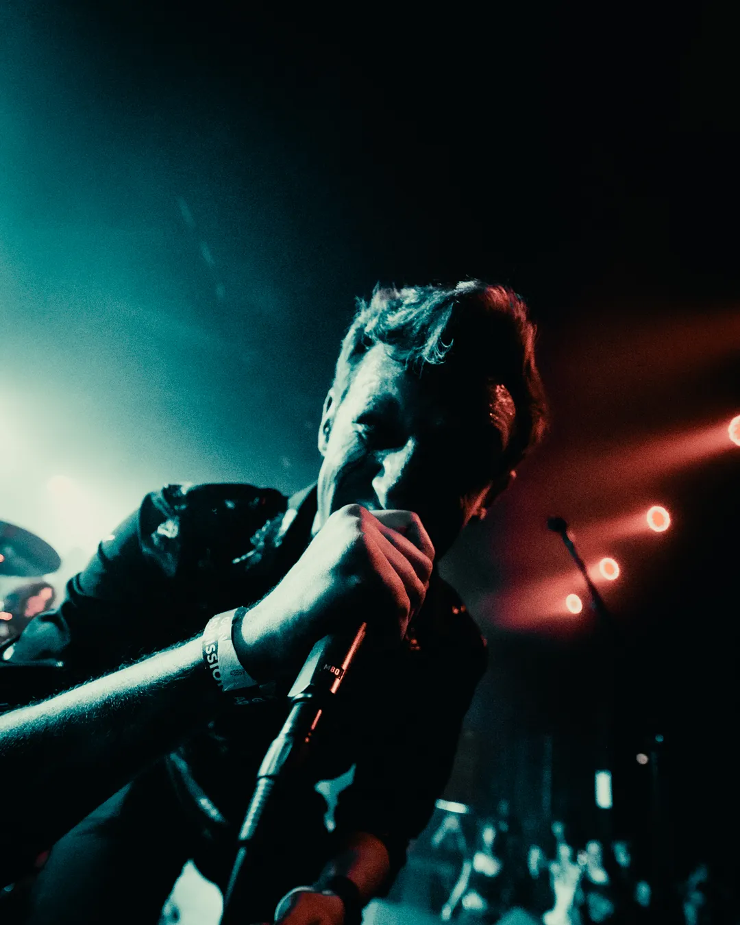 Kyle singing into a microphone on stage under teal and red stage lights